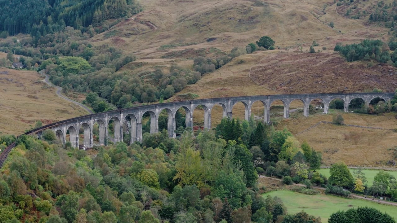 Vinklet nedover, sirkler mot høyre av Glenfinnan viadukt som avslører frodig landskap og løvverk.