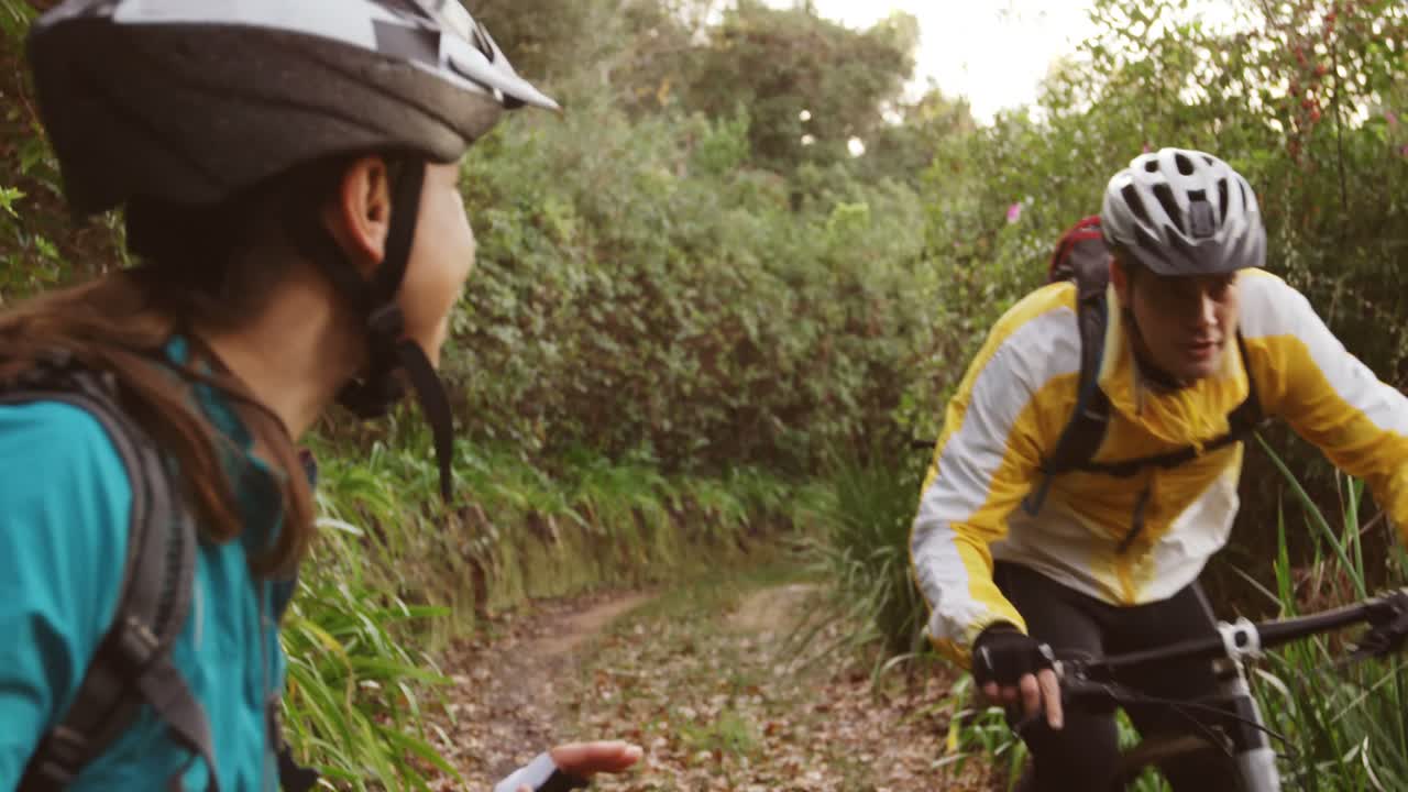 Homem andando de bicicleta enquanto mulher torce na floresta