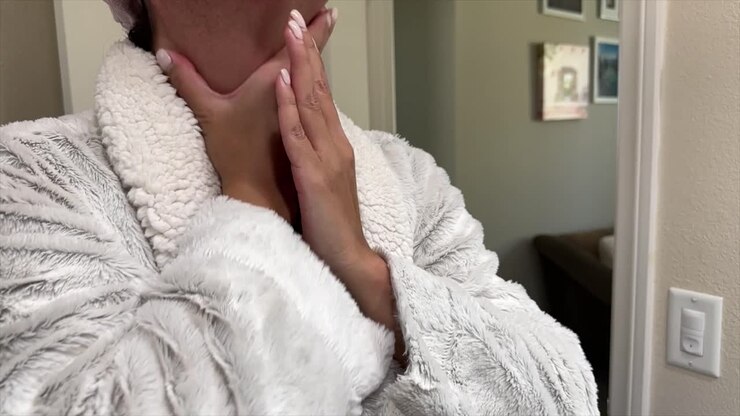 Donna latina in accappatoio che applica fondotinta liquido, senza il viso in primo piano.