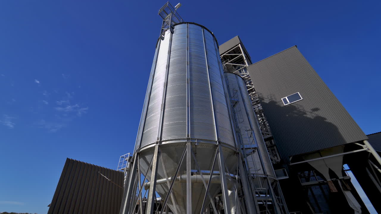 Modern silos on blue sky background. Large silver grain elevator outdoors. Industrial territory of warehouse. Agricultural storage and processing plant.