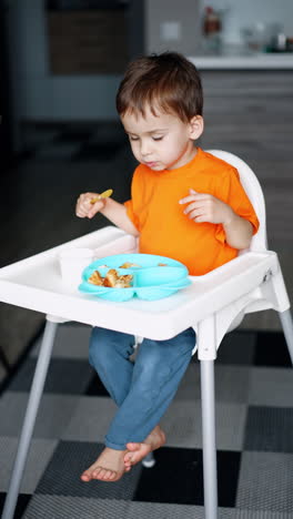 happy toddler boy sits at high chair clapping his feet. cheerful baby is eating dairy from a cup. vertical video.