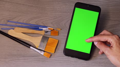 close-up of a woman's hand holding green mock-up screen smartphone. modern mobile phone. brushes of painting on the background. copy space. chroma key