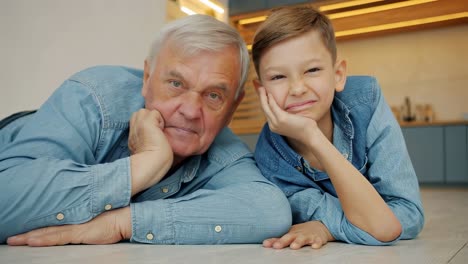 grandfather and grandson are lying on the floor, wearing matching denim shirts, resting their heads on their hands, creating a heartwarming scene of familial bonding