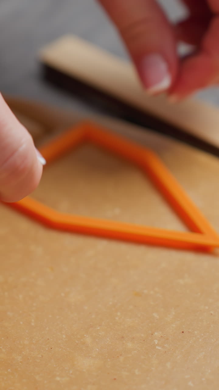 primer plano de las manos de la mujer presionando un cortador de galletas naranja en masa marrón, creando formas precisas, uñas cuidadosas, preparación para hornear, encimera texturizada, guías de madera e iluminación suave