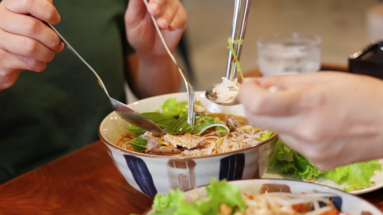 Cận cảnh thực khách cùng thưởng thức bát bún phở Việt Nam với rau thơm tươi và thịt lợn