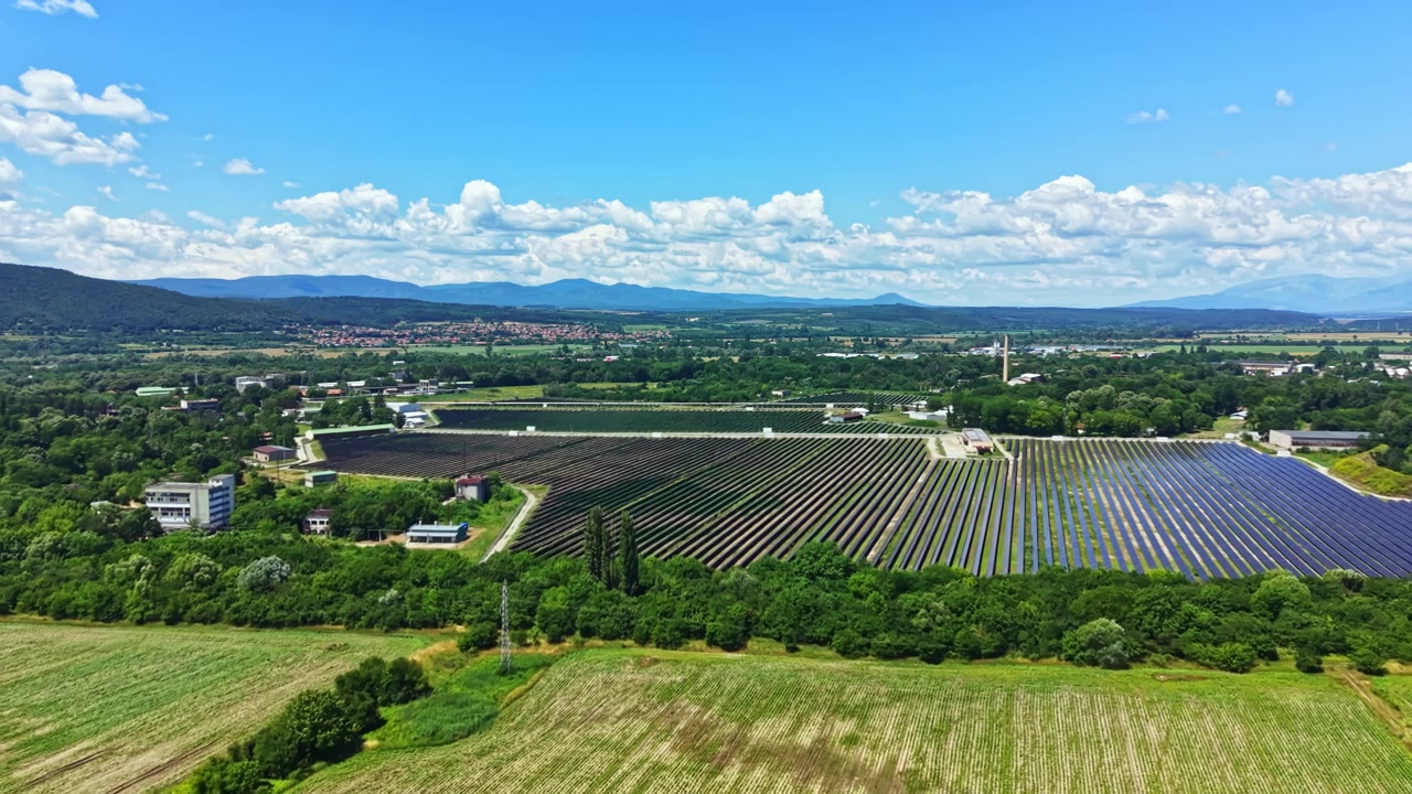 晴れた日の田園地帯、遠くの山々を望む谷の近くの畑にソーラーパネルが広がっています。