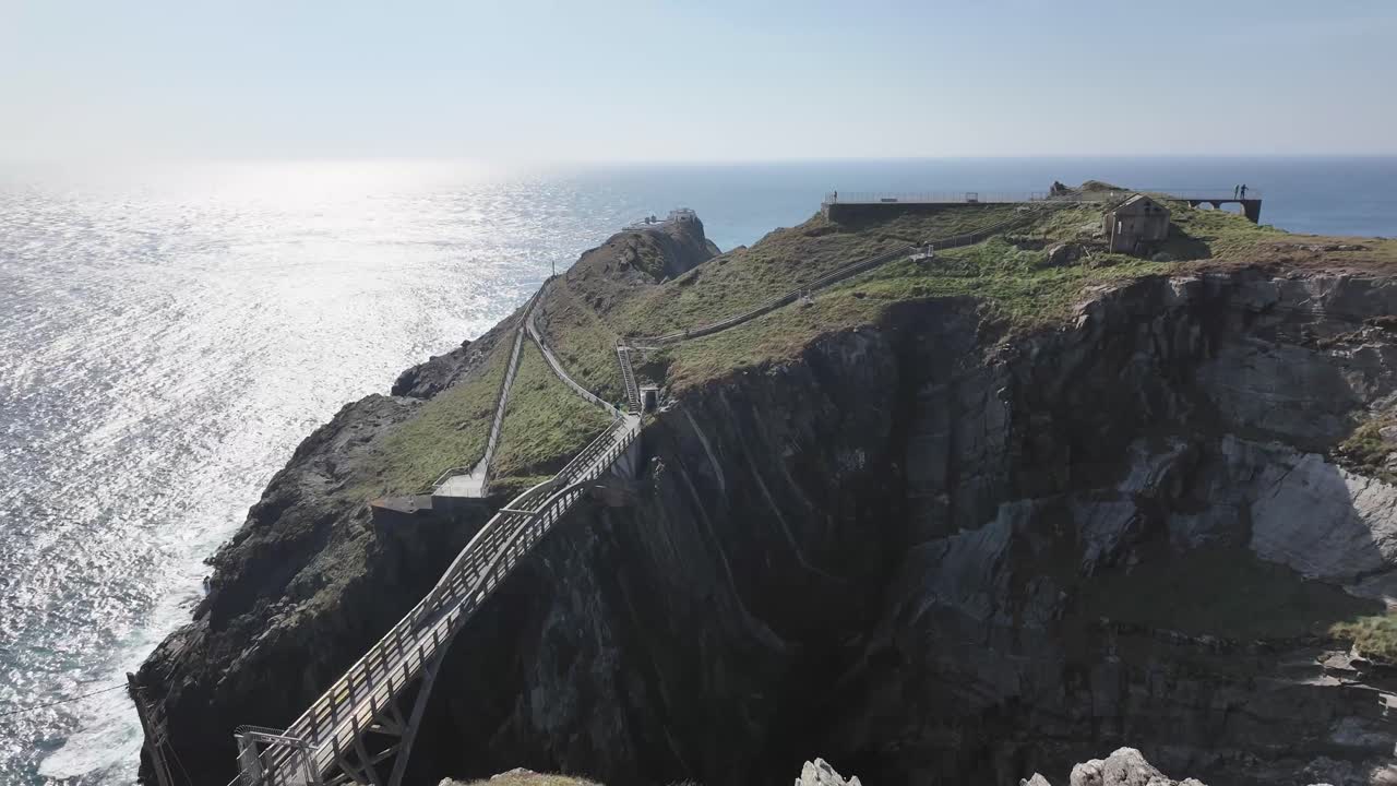 Dramatic landscape with arched bridge across precipices, shimmering ocean and Mizen Head lighthouse, the view from visitors platform. West Cork Ireland