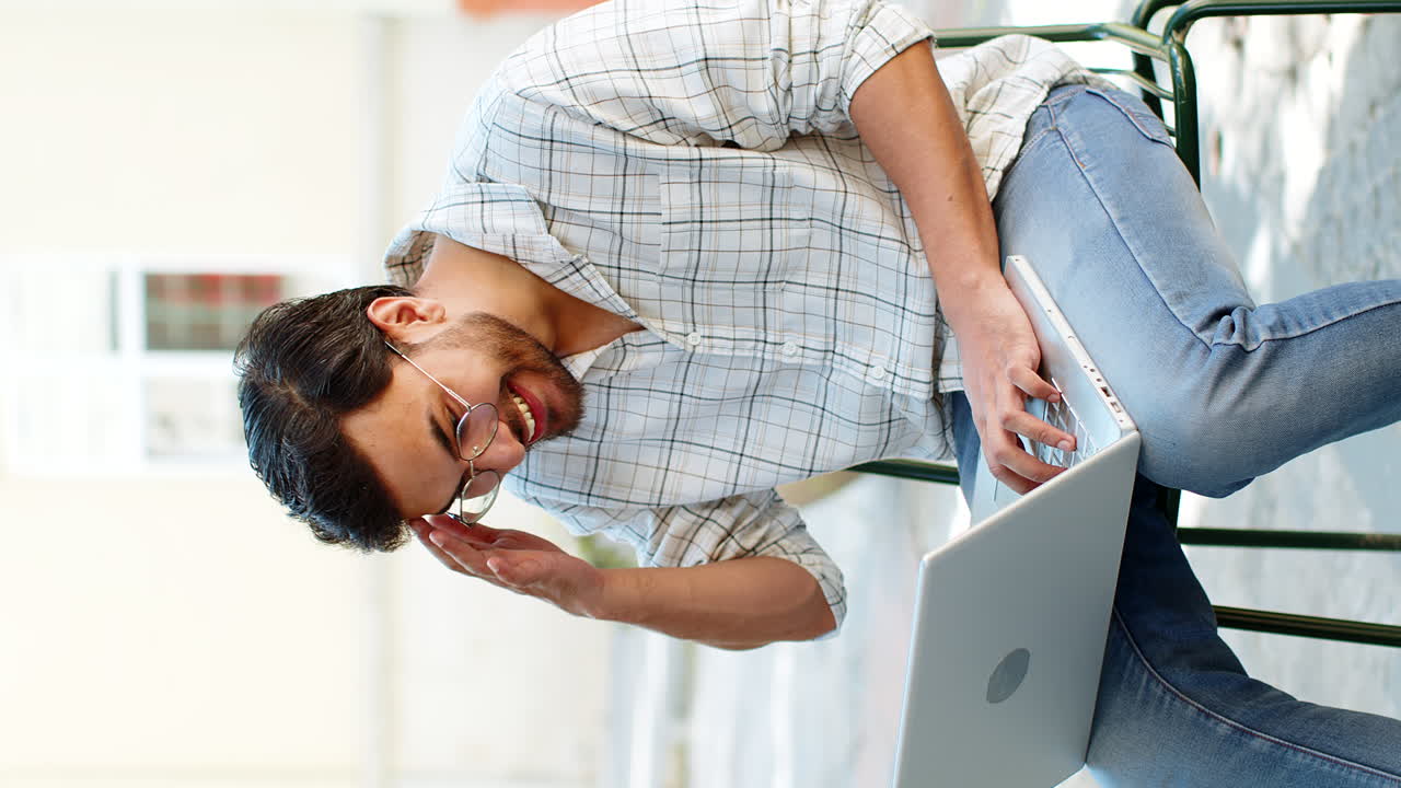 Indian young man using laptop computer celebrating win good message news sitting on chair outdoors