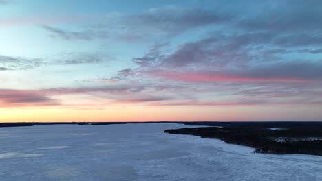 Aerial-footage-over-a-frozen-lake-revealing-majestic-clouds-at-sunset