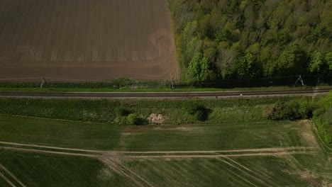 Drohnenaufnahmen-Eines-Zuges,-Der-Durch-Eine-Landschaft-Mit-Feldern-Auf-Beiden-Seiten-Der-Gleise-Fährt