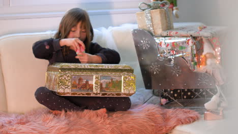 surprised and excited young girl opening box with presents in front of christmas decoration with gifts and packages on santa sledge