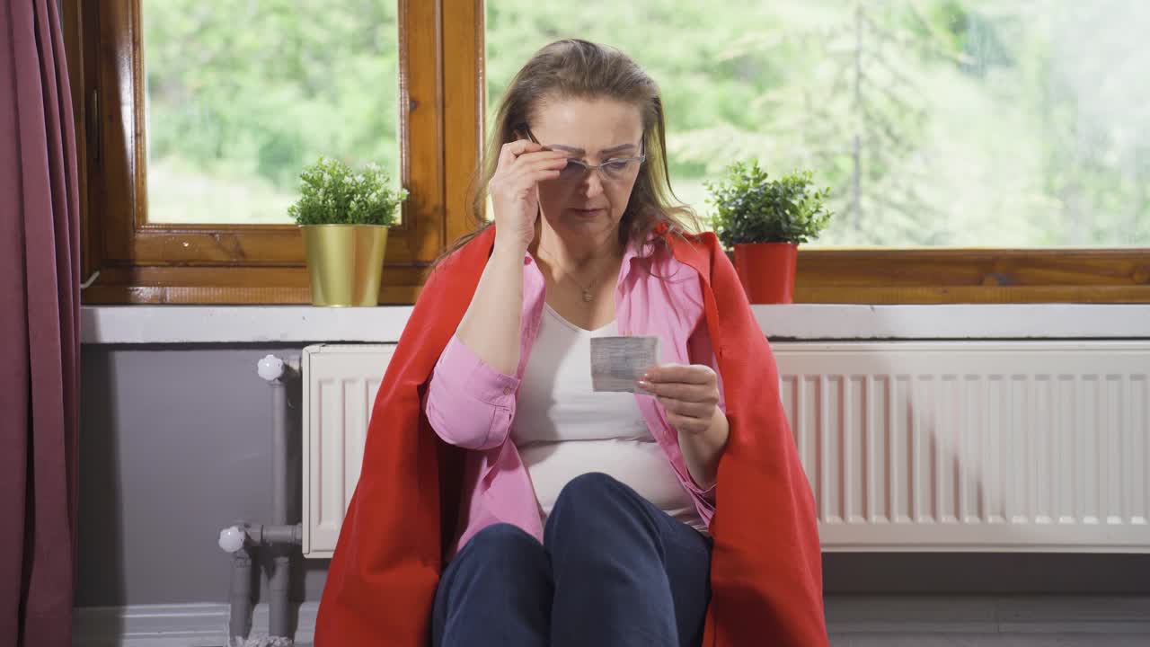 mujer apoyada en el calentador mirando la factura alta.