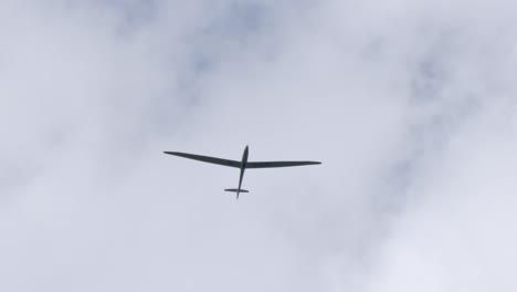 looking up at glider soaring through the sky with clouds overhead