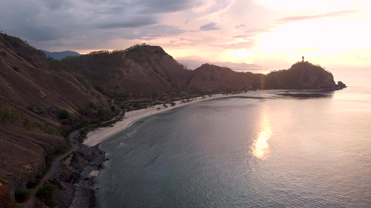 Dominando una playa de bahía curva y recóndita, paisaje de colinas y la estatua del Cristo Rey en una isla tropical en Dili, Timor Oriental.