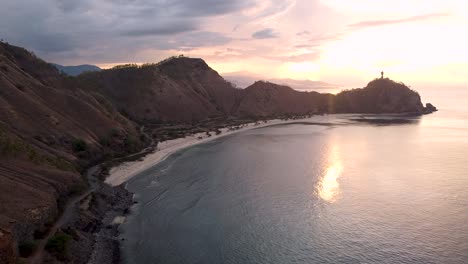 elevándose sobre una playa aislada de la bahía curva, un paisaje montañoso y una estatua de cristo rei jesucristo en una isla tropical en dili, timor leste