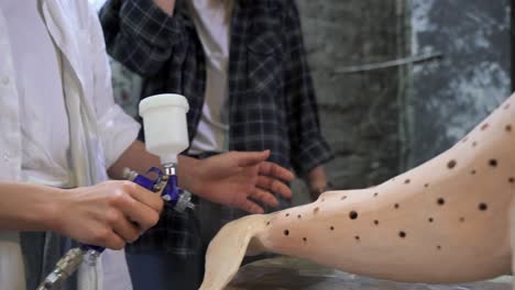 dos mujeres pintando una escultura de ballena de madera en un estudio de arte