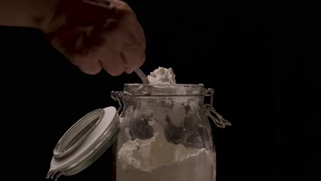 taking flour from a jar with a tablespoon close up on a black backdrop