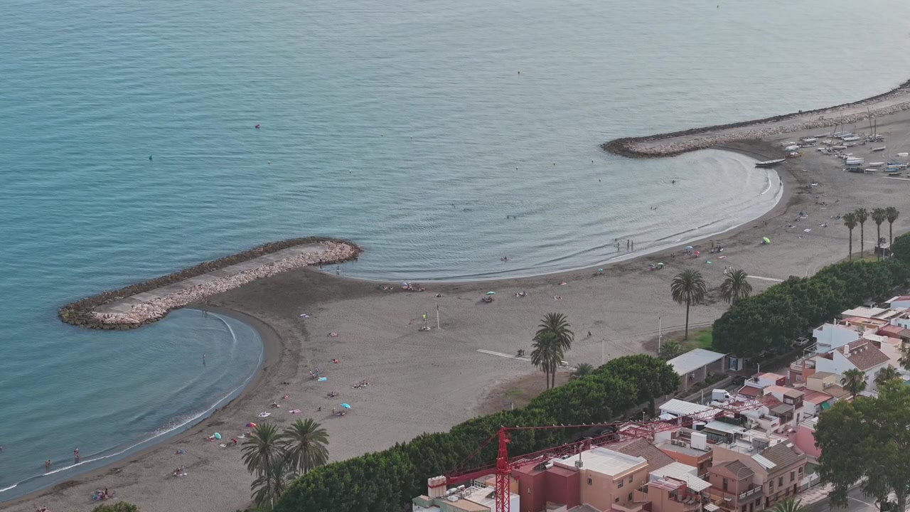 Vista aerea della spiaggia di Malaga, Spagna, con frangiflutti curvi, acque calme del Mediterraneo e litorale urbano, che cattura l'ingegneria costiera, il turismo e lo stile di vita balneare