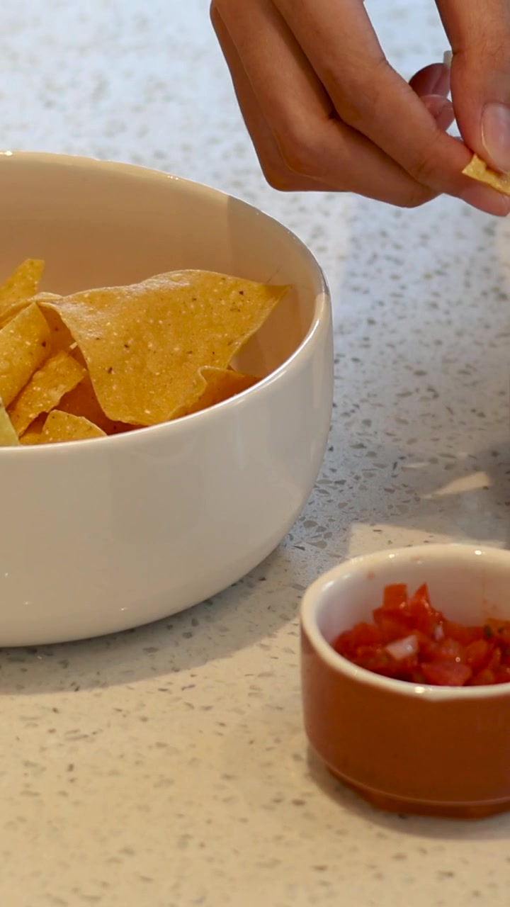 Mani che aggiungono salsa ai nachos in una ciotola