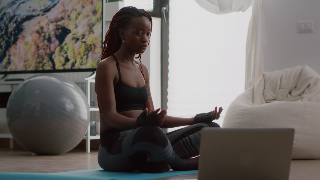 Slim black woman sitting in lotus pose on yoga map with closed eyes