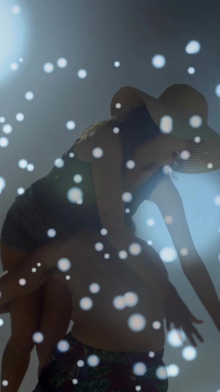Aggiustando il cappello, inizia il sollevamento: la donna sposta il peso e l'uomo la solleva sulla schiena, con cielo retroilluminato, effetto bokeh e pubblicità.