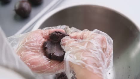 manos con guantes desechables están haciendo bolas de cacao caseras rellenas con cubos de chocolate oscuro y colocándolas en una bandeja.