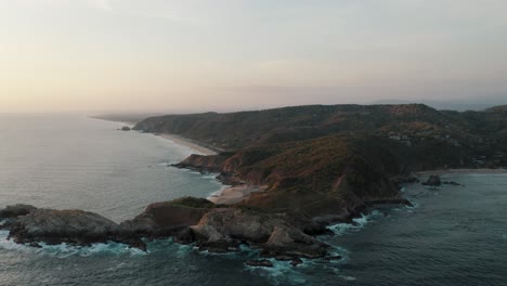 Toma-épica-De-Drones-De-La-Playa-Mazunte-Bordeada-Por-Punta-Cometa,-Que-Es-Una-Pequeña-Península-O-Montaña-Que-Sobresale-De-La-Costa,-México-Durante-La-Puesta-De-Sol