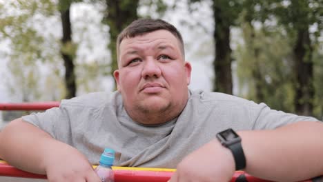 pensive concentrated fat young man in gray tshirt standing near horizontal bar outdoors pensive concentrated fat young man in gray tshirt standing near horizontal bar outdoors a break during training stop struggle with excess weight