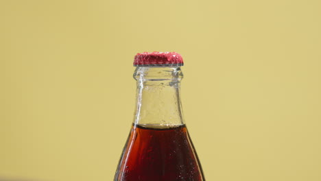 fotografía de cerca de una persona recogiendo una botella de cerveza fría o bebida gaseosa con tapa de metal y gotas de condensación