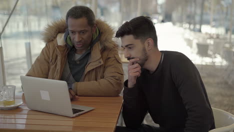 Focused-multiethnic-men-using-laptop-in-cafe