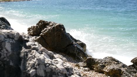 rocky beach on corfu island with foamy waves crashing into a cliff