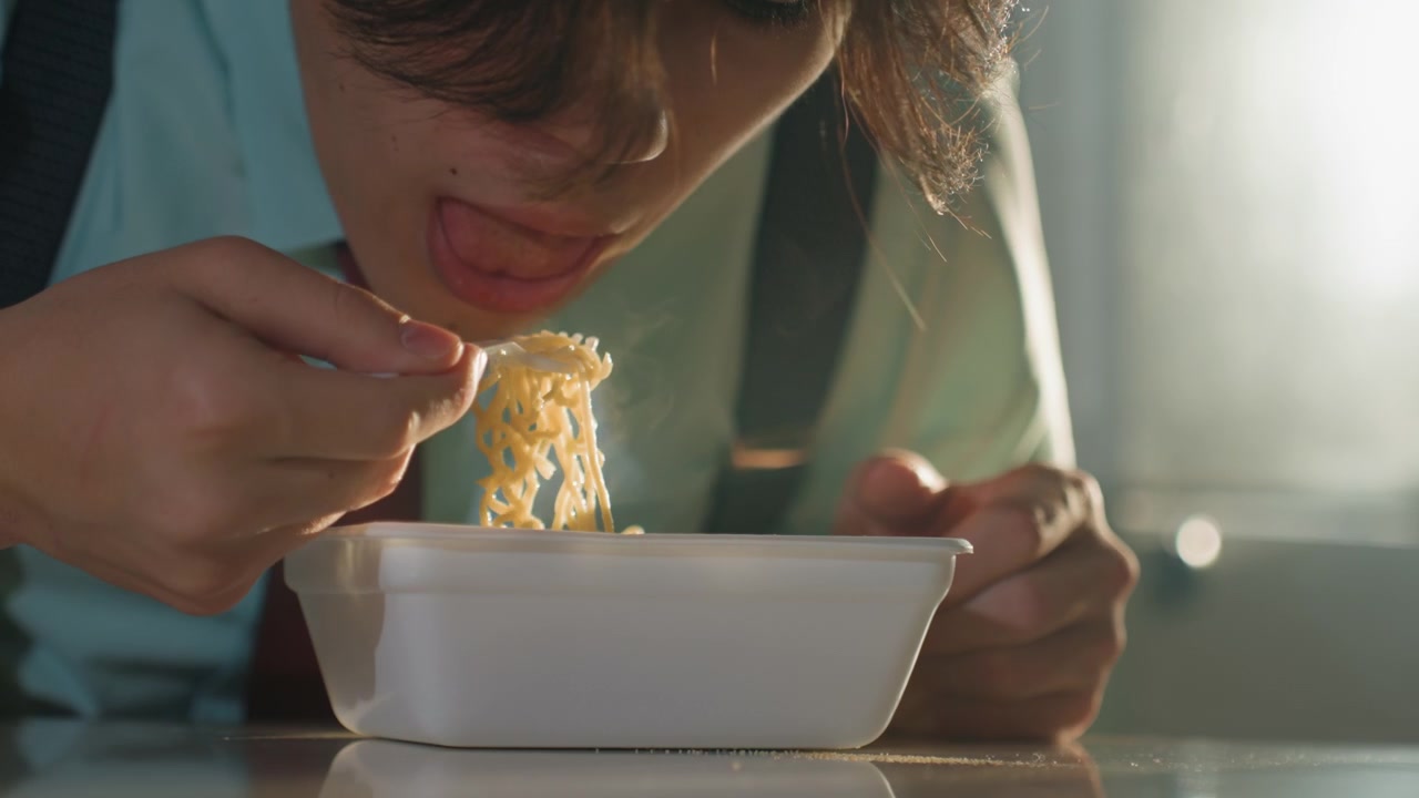 Asian man stirring noodles closeup savoring flavor, hands and disposable fork in frame, steam and texture visible, concentrated bite and expressive relief, warm cinematic glow and intimate detail
