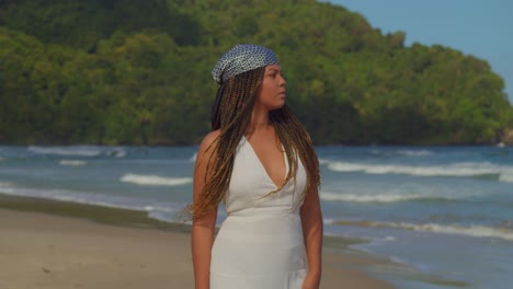 Young-girl-in-a-beach-dress-walking-on-the-golden-sands-of-a-tropical-beach-with-waves-of-the-ocean-crashing-in-the-background