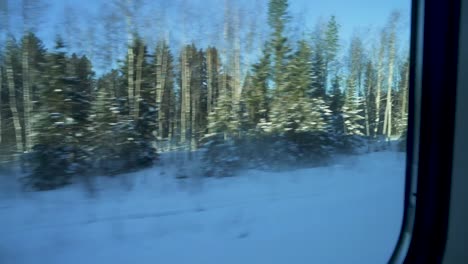 Traveling-by-train-through-a-snowy-forest,-passing-homes-with-snow-covered-roofs