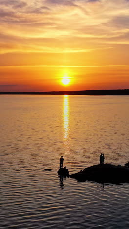 view from a drone on the river in the evening. people stand on long stones situated in water at sunset. camera moves forward. vertical video