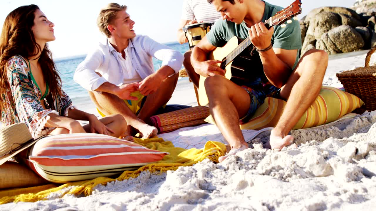 hombre tocando la guitarra para amigos sentado en la playa 4k