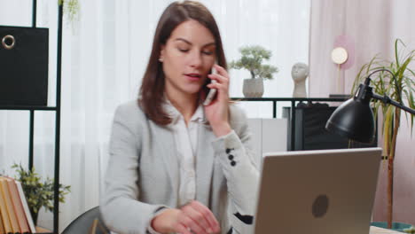 Operadora-De-Mujer-De-Negocios-Comunicándose-Con-El-Cliente-Mediante-Un-Teléfono-Inteligente-Tomando-Notas-En-Documentos-En-Papel