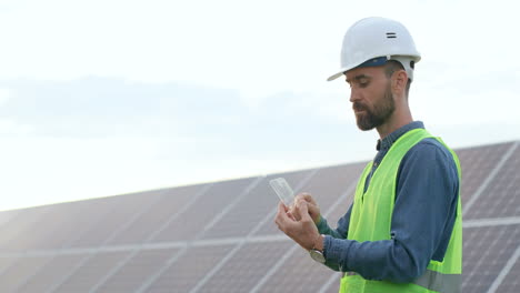 Ingeniero-Masculino-Caucásico-En-Casco-Protector-Usando-Un-Vidrio-Como-Una-Tableta-En-Una-Plantación-Solar