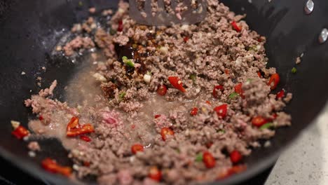 ground beef and red peppers stir-fried in a wok with a spatula, under bright kitchen lighting
