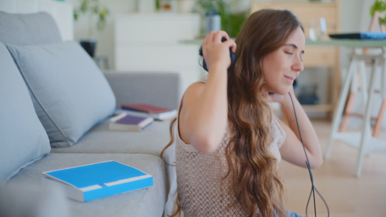 Mujer cierra libro, se pone auriculares para relajarse con música