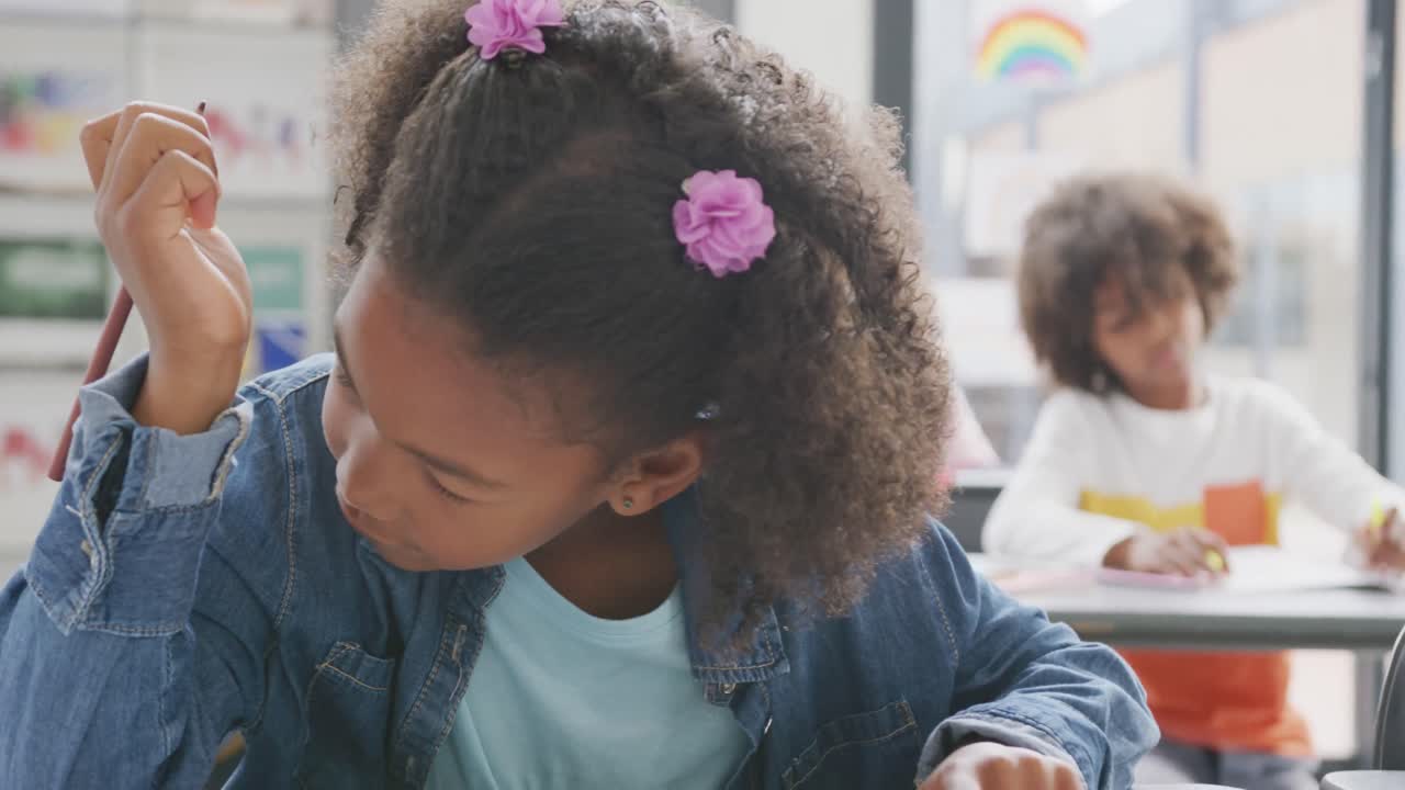 video del retrato de una estudiante biracial feliz sentada en un escritorio trabajando en la clase escolar