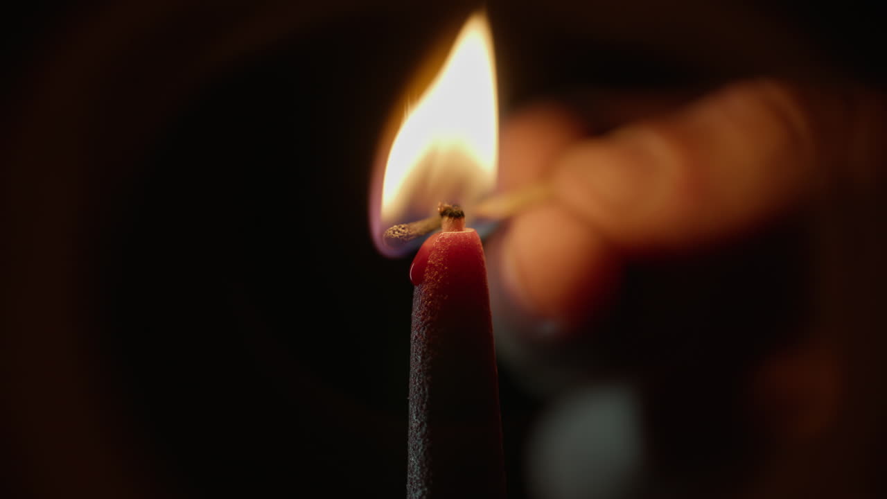 Dita che accendono una candela con un fiammifero su sfondo nero, primo piano. Fiamma brillante