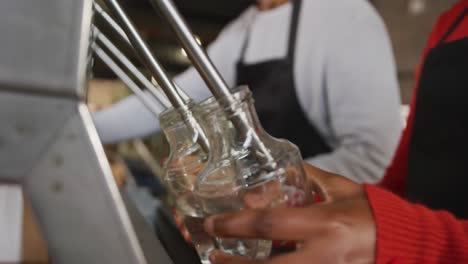 sección media de dos colegas diversos en la destilería de ginebra llenando y sujetando las tapas de las botellas a mano