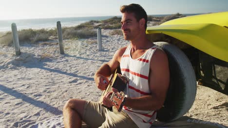 happy caucasian man sitting beside beach buggy by the sea playing guitar