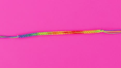 vibrant-close-up-on-threaded-macrame-bracelet,-rainbow-pattern-set-on-pink-background