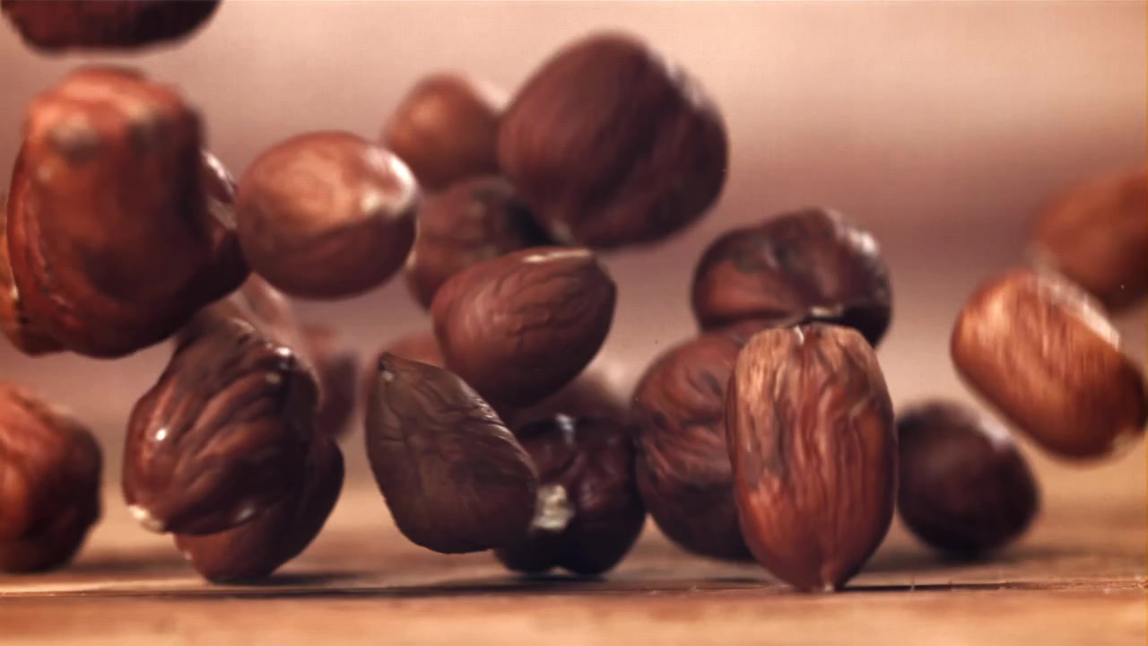 Nocciole sgusciate che cadono al rallentatore su una superficie di legno.