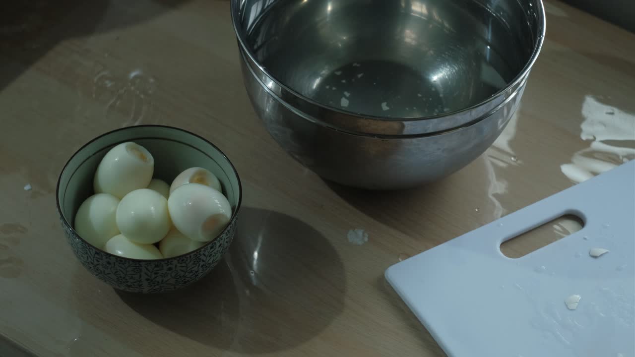 Placing Peeled Boiled Egg In Stainless Steel Bowl In Kitchen. high angle shot