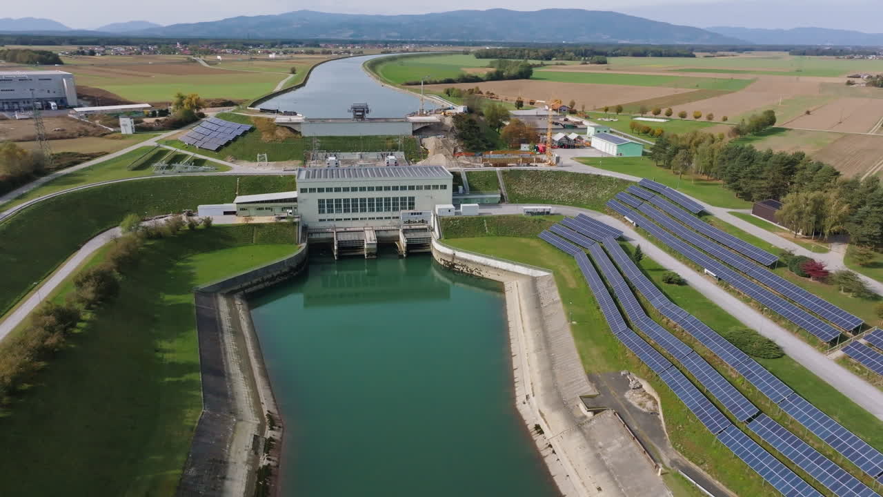 Luchtfoto van een waterkrachtcentrale omgeven door zonnepanelen en groene omgeving, water stroomt