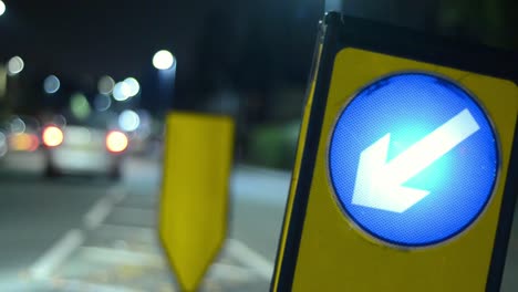 Night-time-road-traffic-sign-pointing-direction-with-traffic-bokeh-as-traffic-passes-by