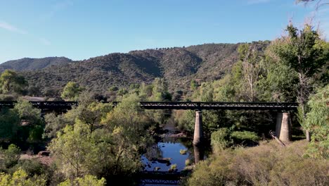 Auto-überquert-Brücke-über-Den-Fluss-Jandula,-Abgelegene-Bewaldete-Landschaft-Der-Sierra-De-Andujar,-Drohnenschub